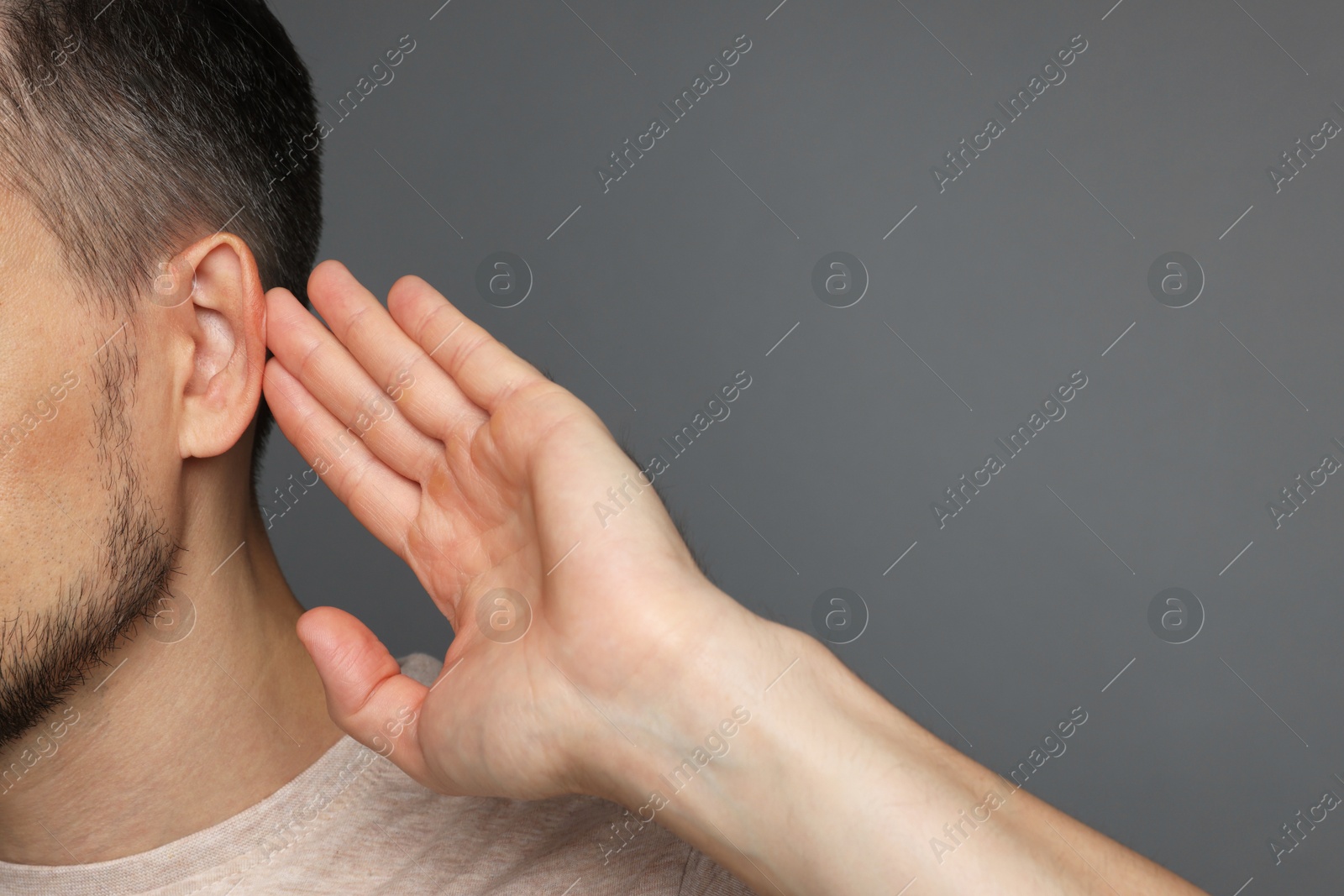 Photo of Man showing hand to ear gesture on grey background, closeup