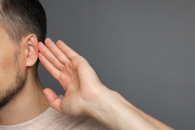 Man showing hand to ear gesture on grey background, closeup