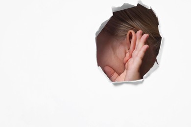 Photo of Little girl showing hand to ear gesture through hole in white paper, closeup. Space for text