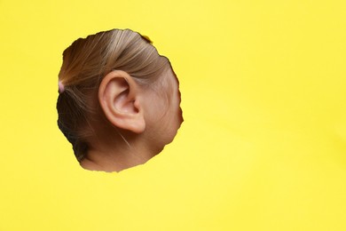 Little girl showing her ear through hole in yellow paper, closeup. Space for text