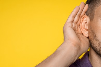 Man showing hand to ear gesture on orange background, closeup. Space for text