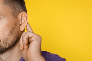 Photo of Man showing hand to ear gesture on orange background, closeup. Space for text