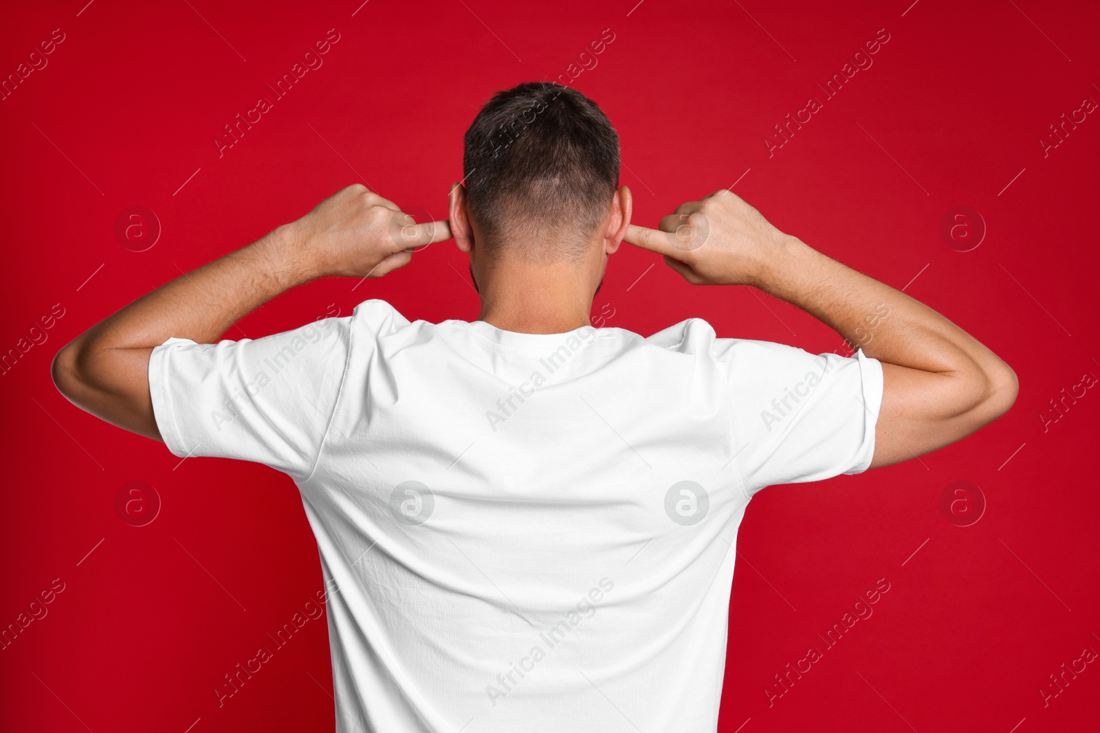 Photo of Man covering his ears with fingers on red background, back view