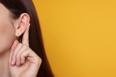 Photo of Woman showing hand to ear gesture on orange background, closeup. Space for text