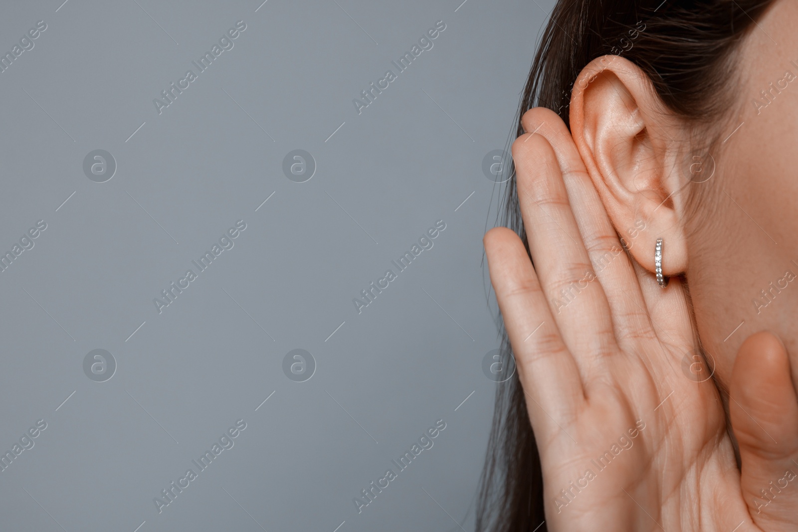 Photo of Woman showing hand to ear gesture on grey background, closeup. Space for text