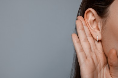 Woman showing hand to ear gesture on grey background, closeup. Space for text