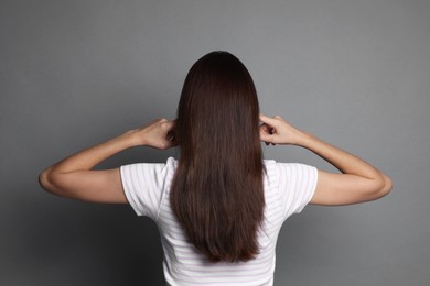 Woman covering her ears with fingers on grey background, back view