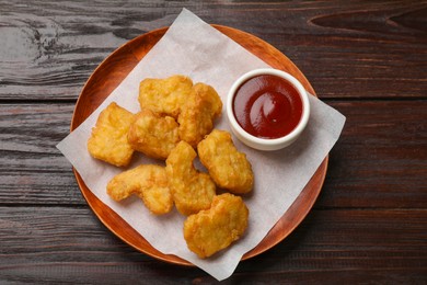 Photo of Delicious chicken nuggets and ketchup on wooden table, top view