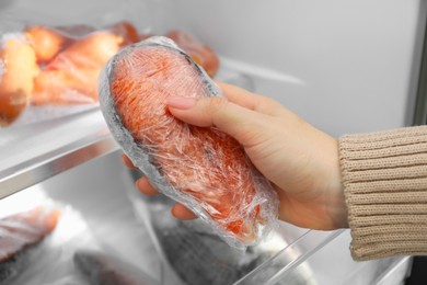 Photo of Woman taking frozen salmon steak out of fridge, closeup