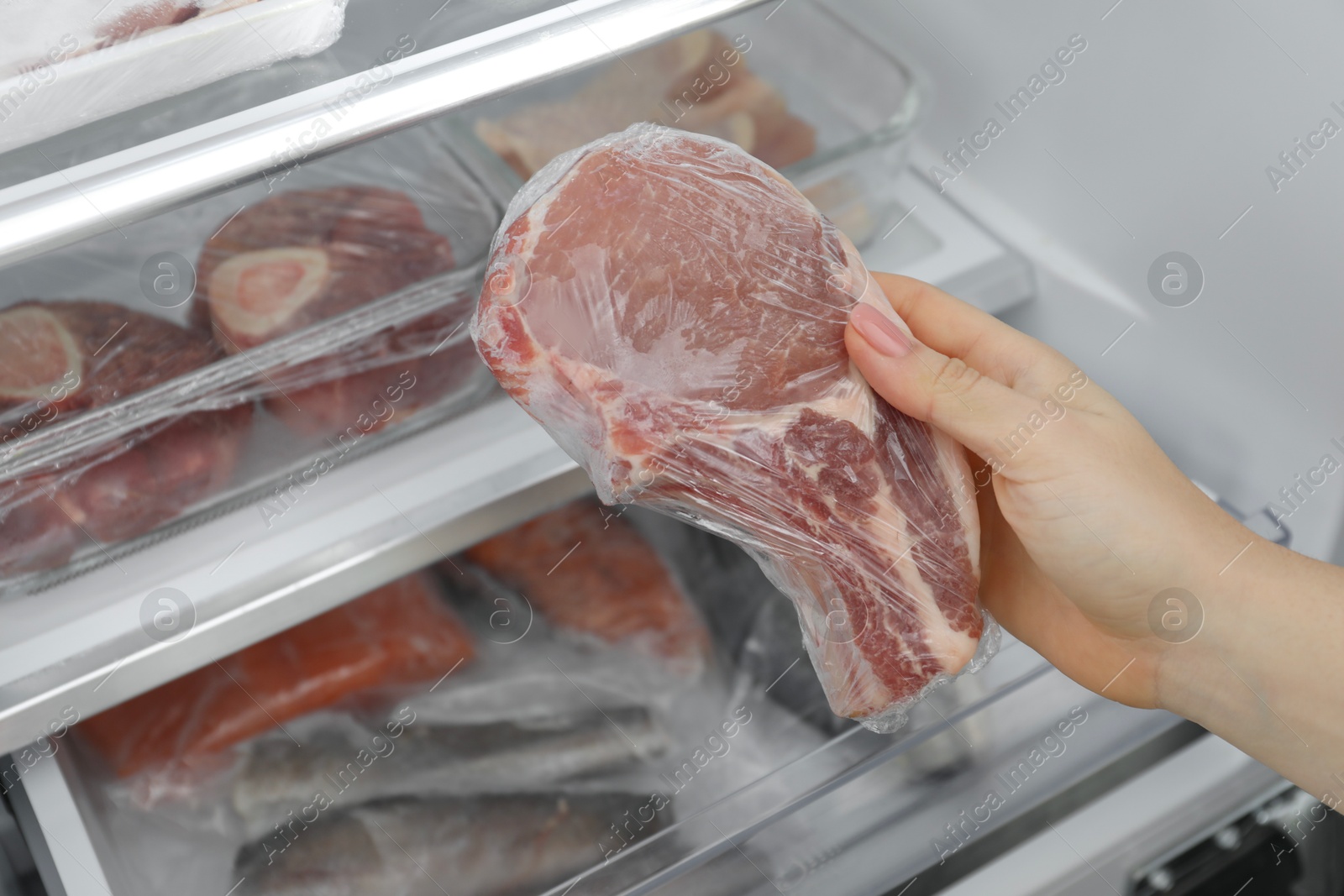 Photo of Woman taking frozen pork steak out of fridge, closeup