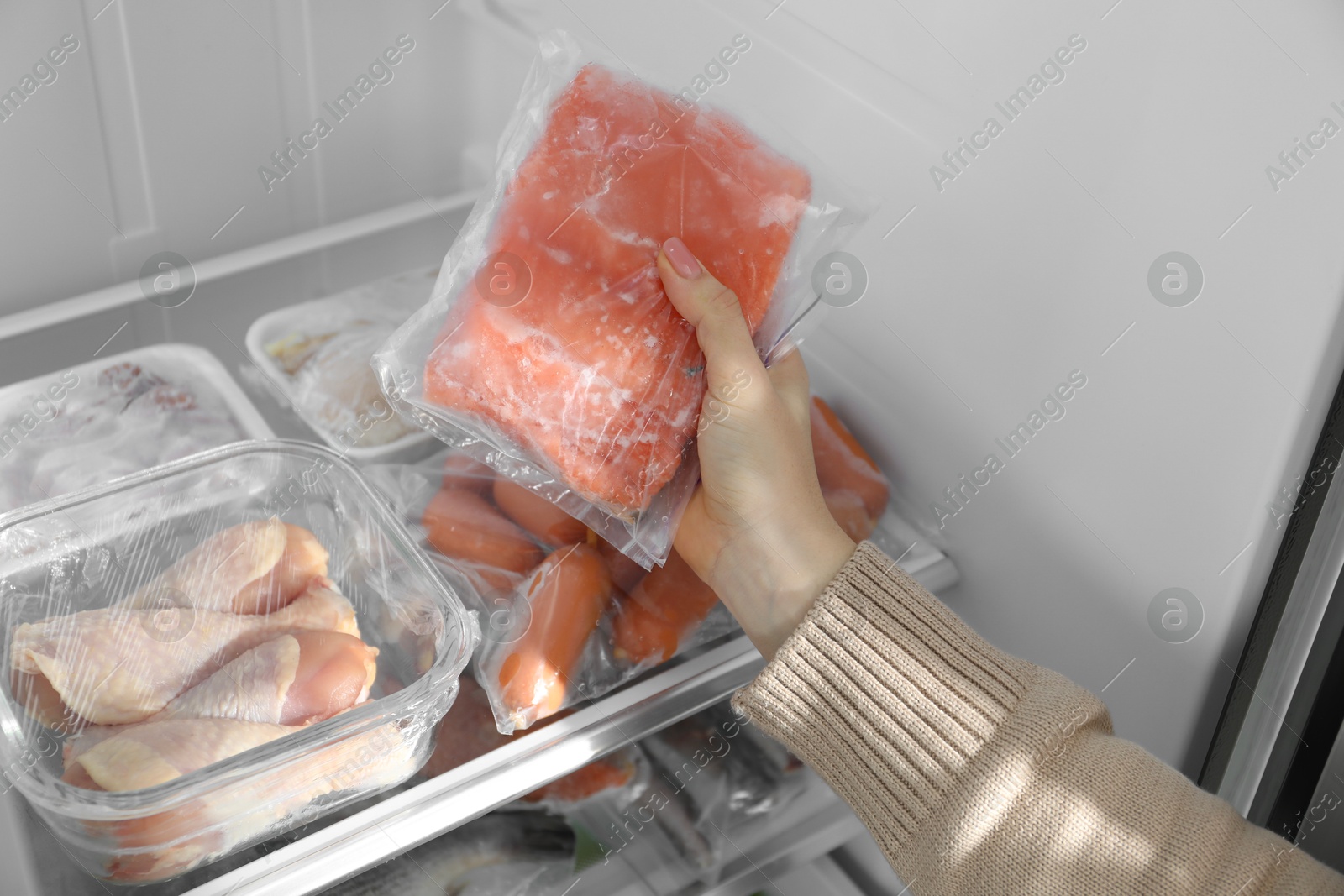 Photo of Woman taking frozen piece of salmon out of fridge, closeup