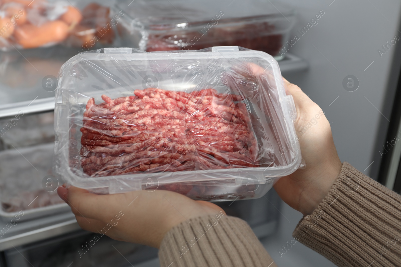 Photo of Woman taking frozen minced meat out of fridge, closeup