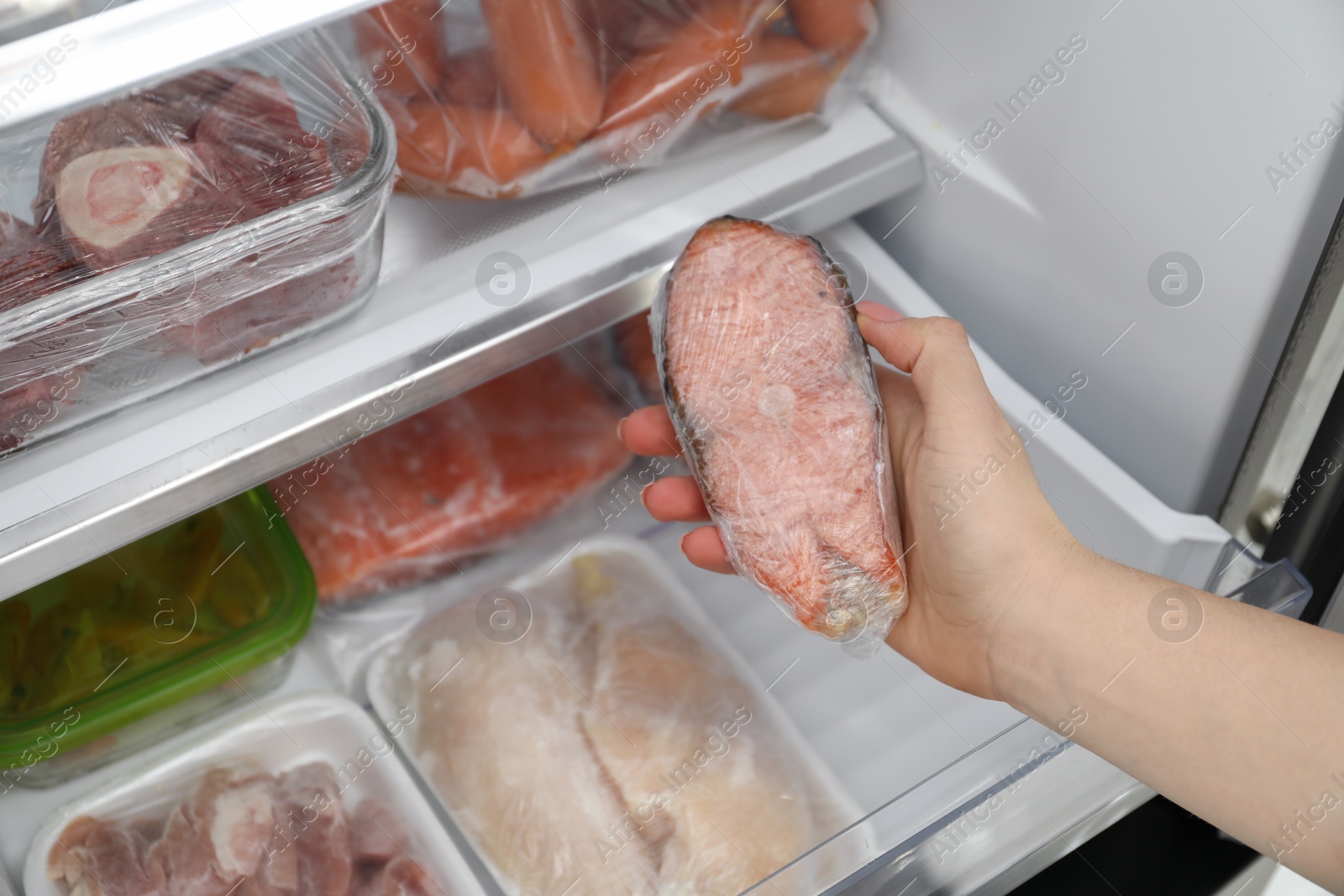 Photo of Woman taking frozen salmon steak out of fridge, closeup