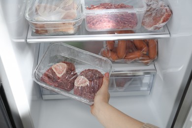 Photo of Woman taking frozen beef steaks out of fridge, closeup