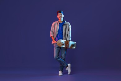 Happy man with skateboard in color lights against blue background