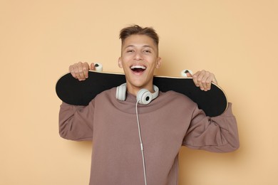 Happy man with skateboard and headphones on beige background