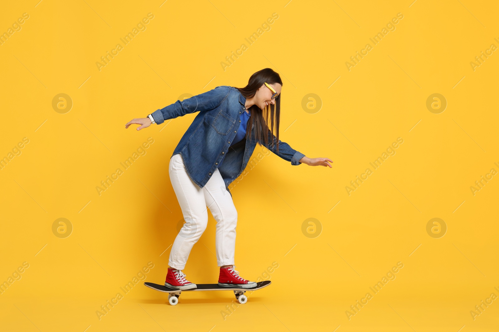 Photo of Smiling woman riding skateboard on orange background