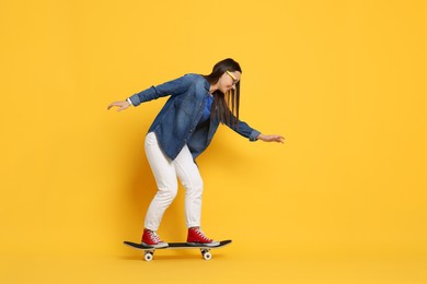 Smiling woman riding skateboard on orange background