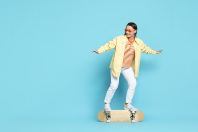 Smiling woman on skateboard against light blue background. Space for text