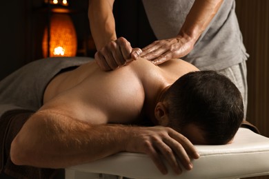 Photo of Professional physiotherapist doing shoulder massage for his client indoors, closeup