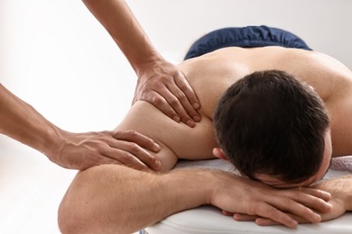 Photo of Professional physiotherapist doing shoulder massage for his client indoors, closeup