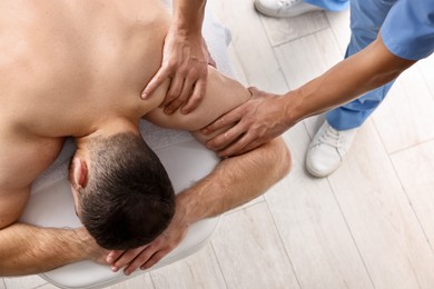 Photo of Professional physiotherapist doing shoulder massage for his client indoors, top view