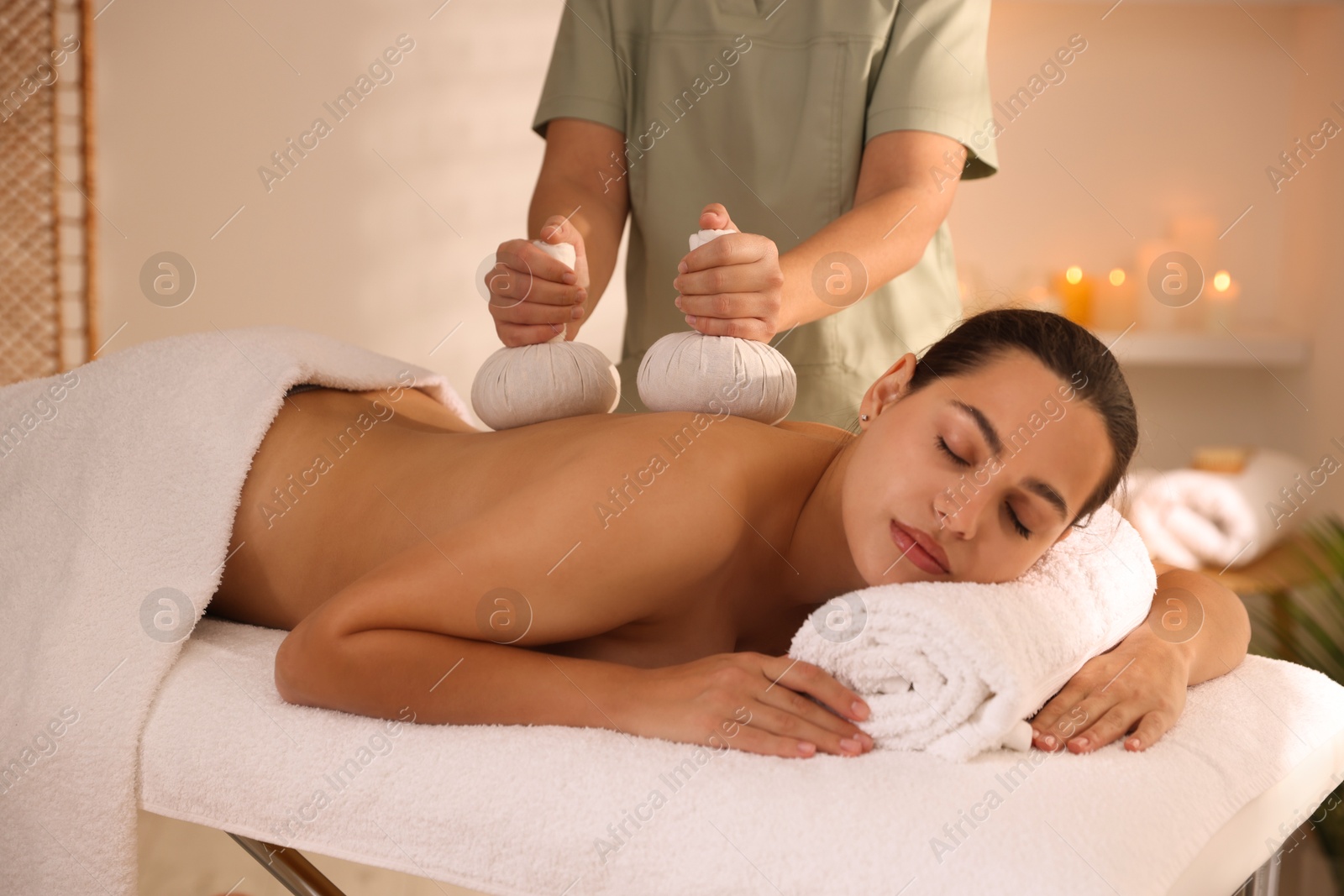 Photo of Woman receiving back massage with herbal bags in spa salon