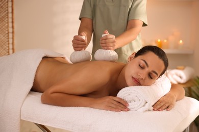 Photo of Woman receiving back massage with herbal bags in spa salon