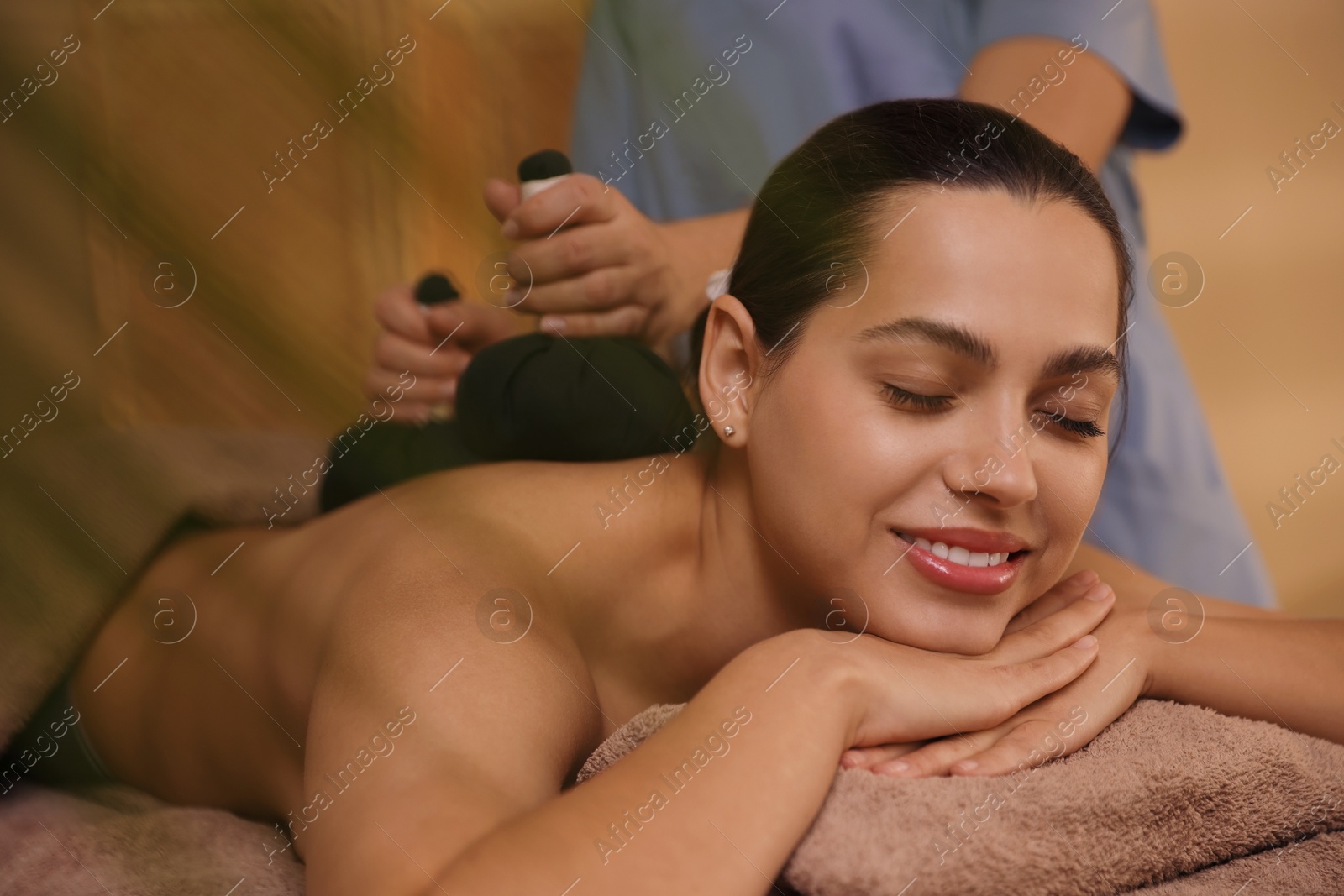 Photo of Woman receiving back massage with herbal bags in spa salon