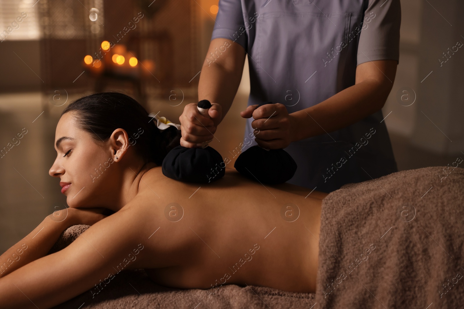 Photo of Woman receiving back massage with herbal bags in spa salon