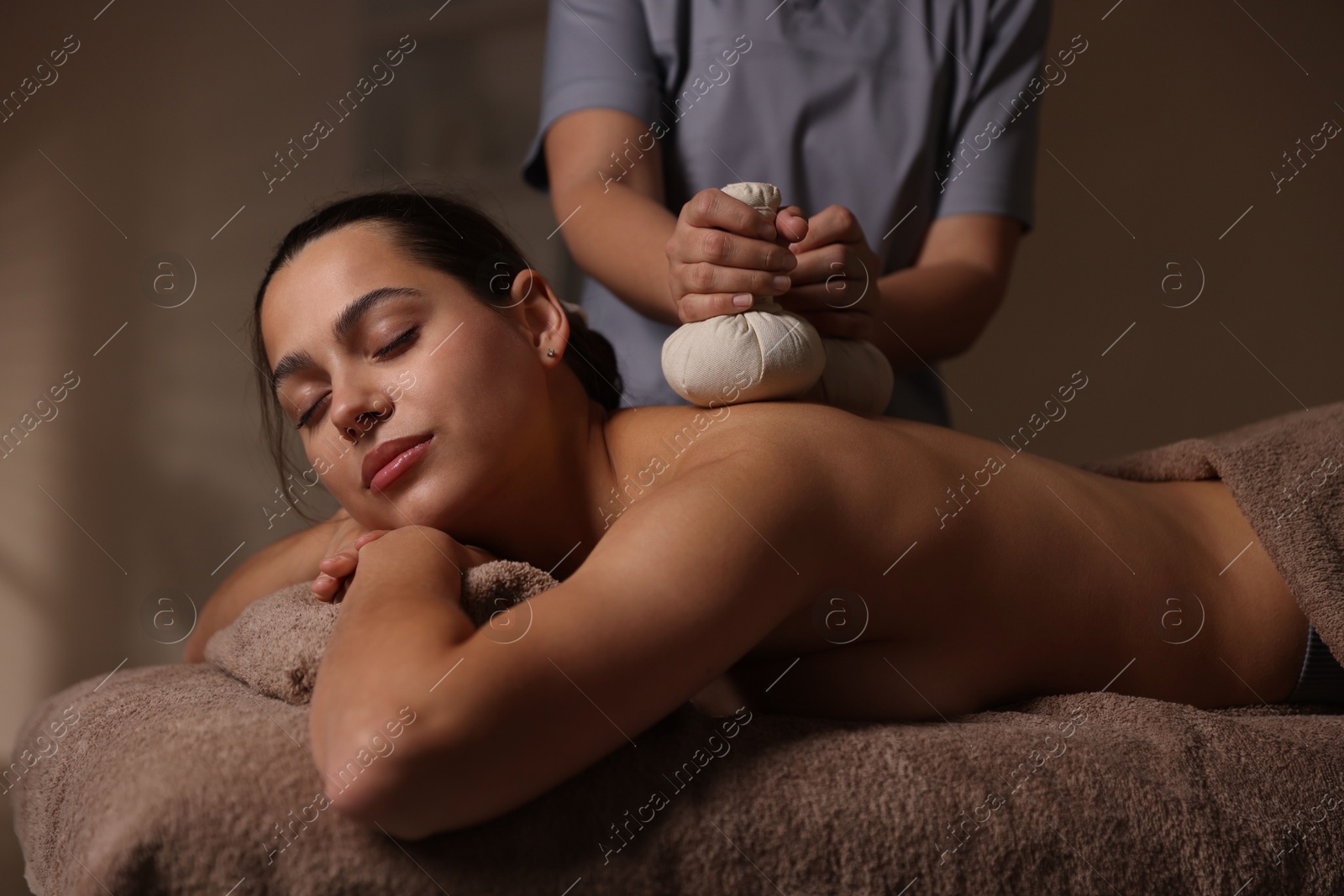 Photo of Woman receiving back massage with herbal bags in spa salon