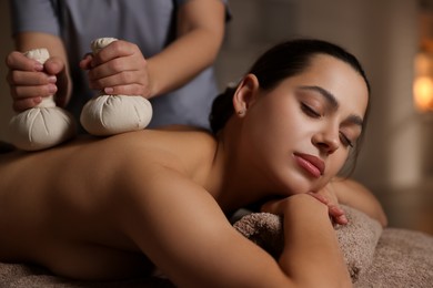 Photo of Woman receiving back massage with herbal bags in spa salon