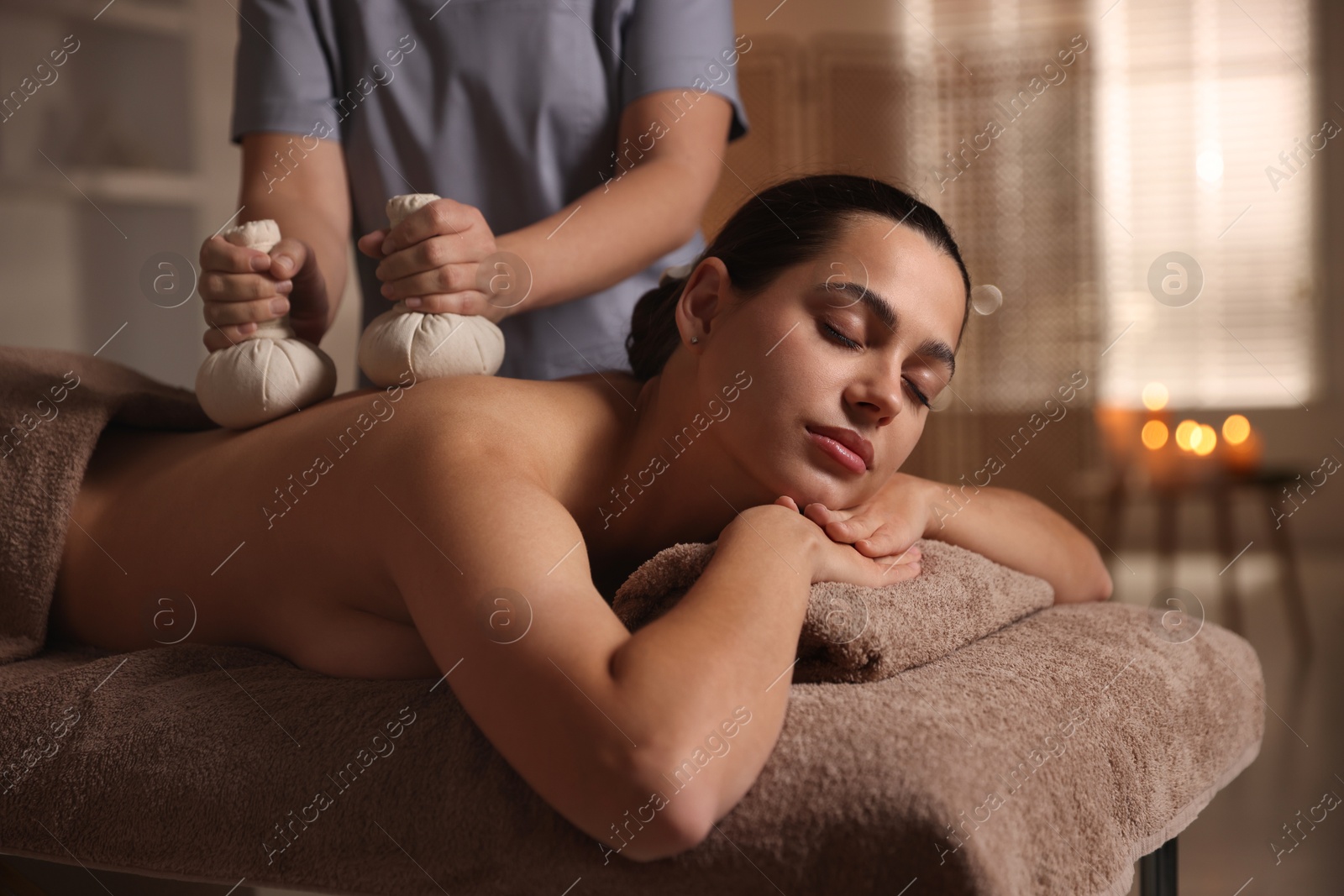 Photo of Woman receiving back massage with herbal bags in spa salon