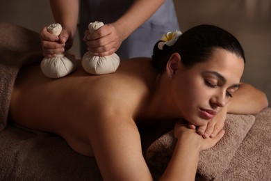 Photo of Woman receiving back massage with herbal bags in spa salon