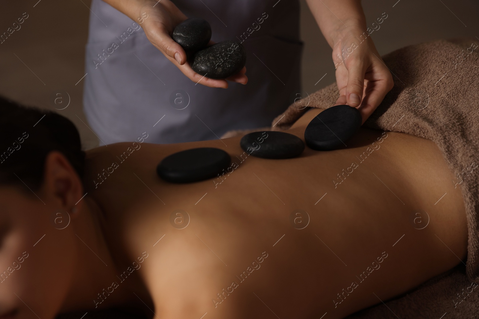 Photo of Woman receiving hot stone massage in spa salon, closeup