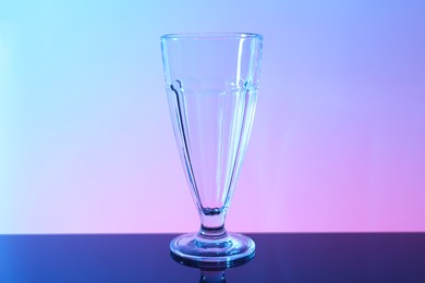 Photo of One empty glass on table against color background