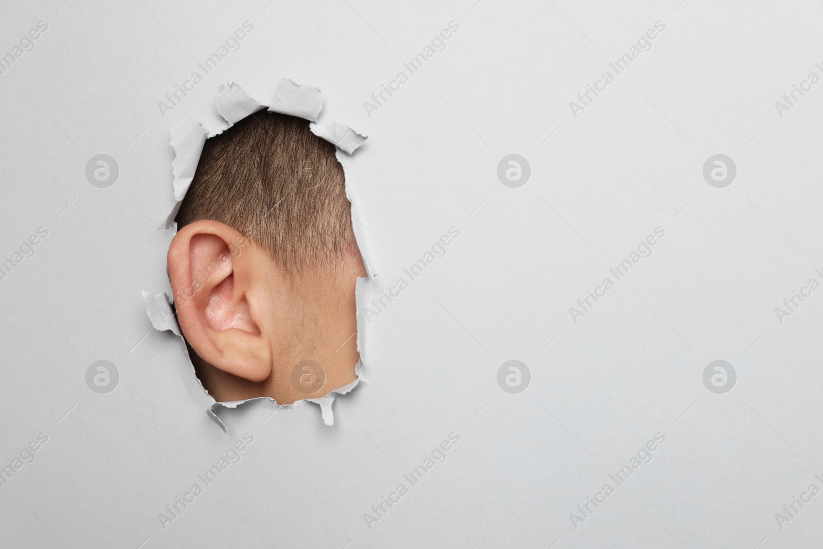 Photo of Man showing his ear through hole in grey paper, closeup. Space for text