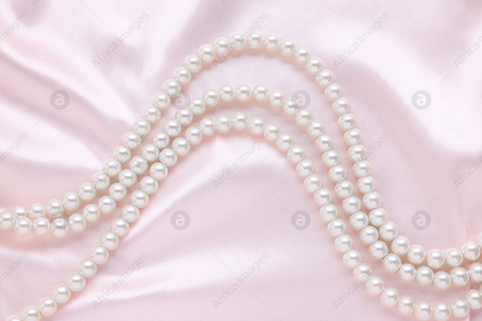 Photo of Elegant pearl necklace on pink fabric, top view