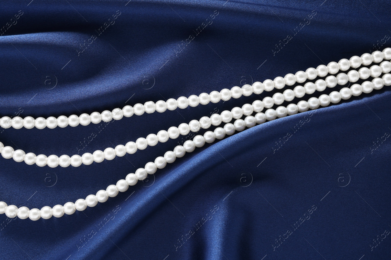 Photo of Elegant pearl necklace on dark blue fabric, top view