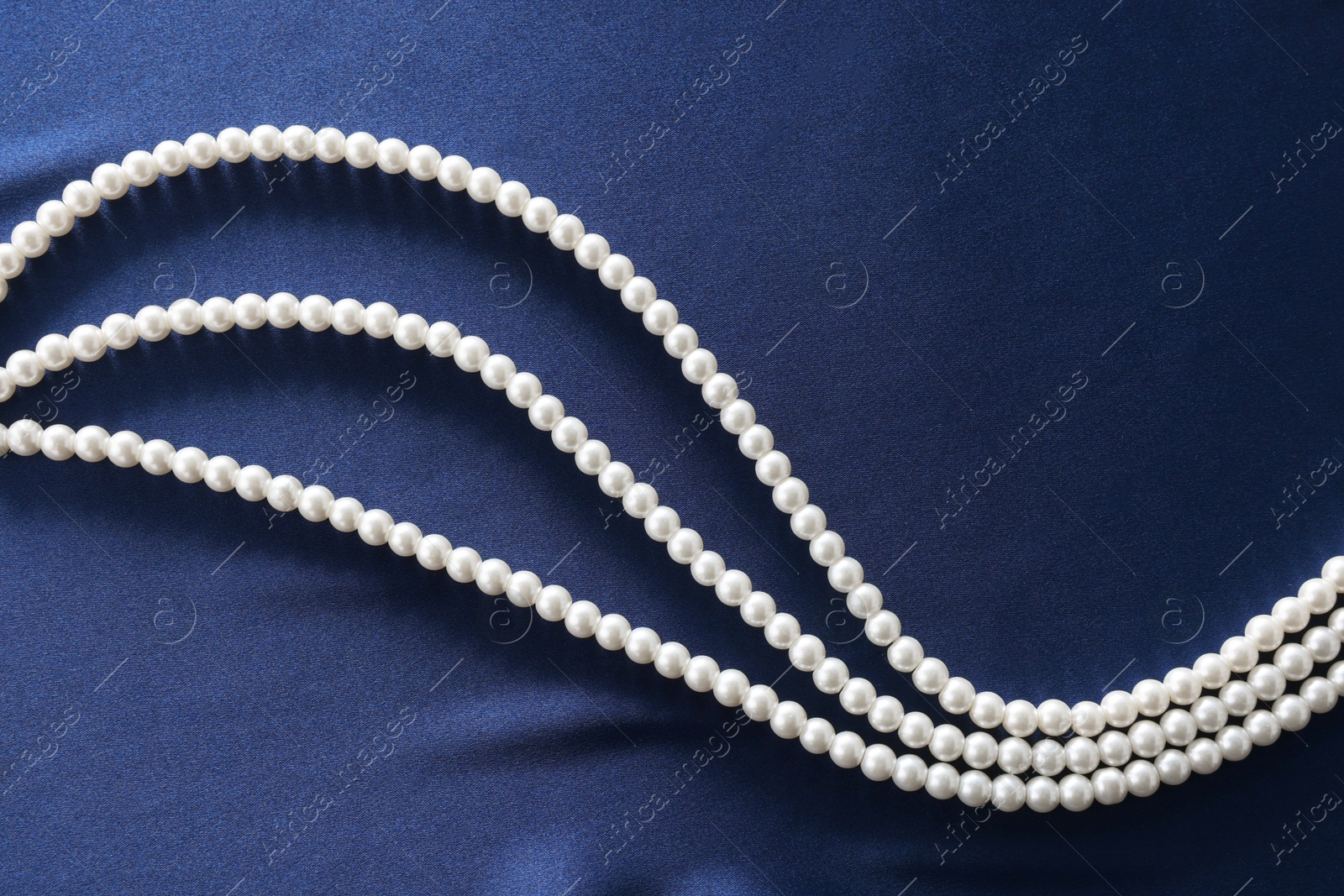 Photo of Elegant pearl necklace on dark blue fabric, top view