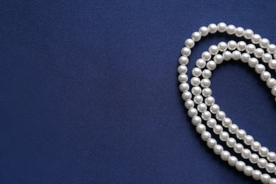 Photo of Elegant pearl necklace on dark blue fabric, top view. Space for text