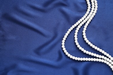 Photo of Elegant pearl necklace on dark blue fabric, top view. Space for text