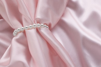 Photo of Elegant pearl bracelet on pink fabric, closeup. Space for text