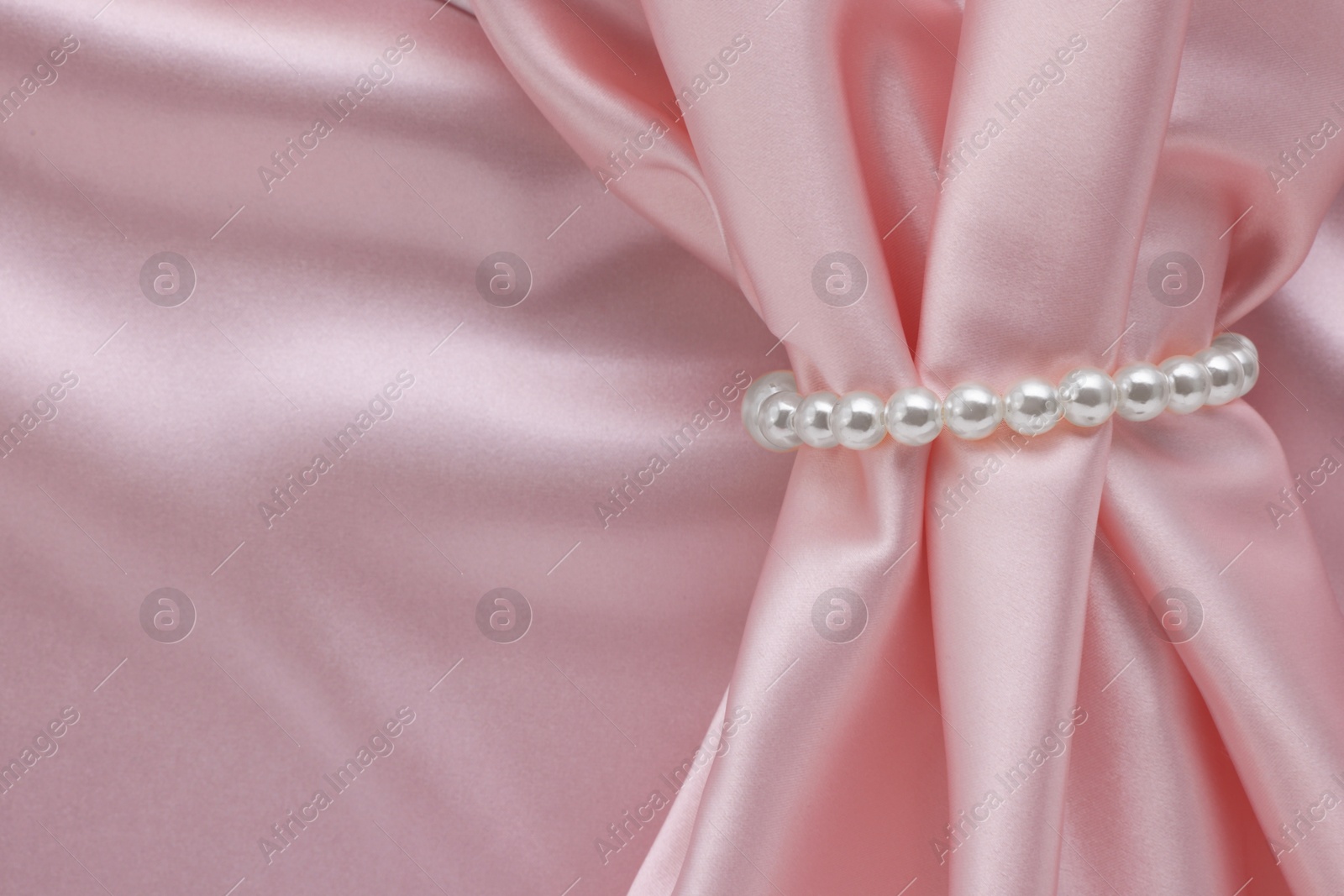 Photo of Elegant pearl bracelet on pink fabric, top view. Space for text