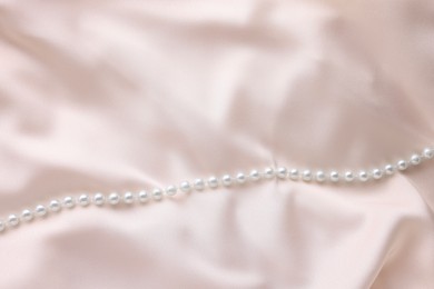 Photo of Beautiful pearl necklace on beige cloth, top view. Space for text