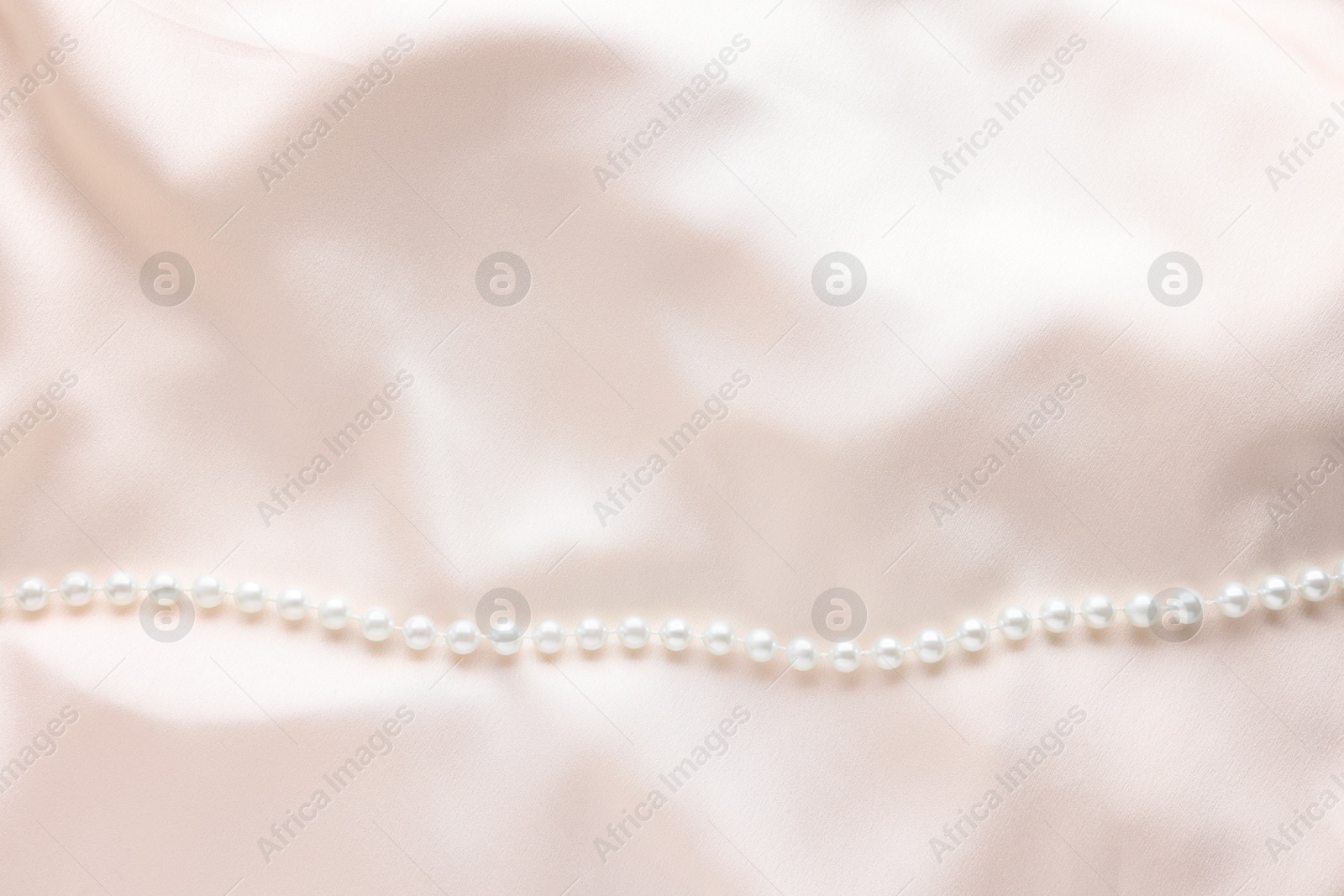 Photo of Beautiful pearl necklace on beige cloth, top view. Space for text