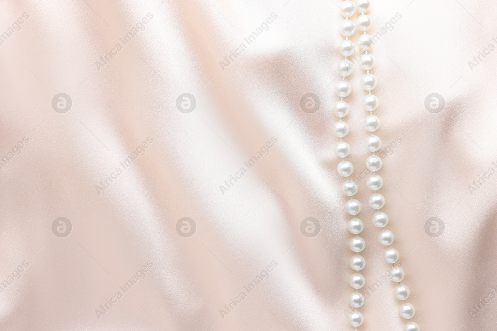 Photo of Beautiful pearl necklace on beige cloth, top view. Space for text