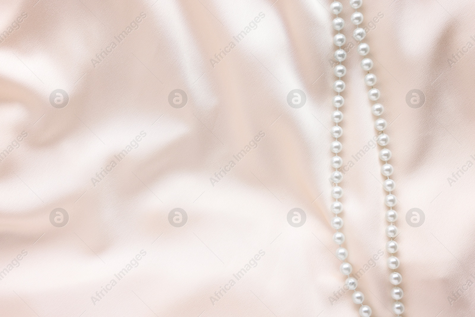 Photo of Beautiful pearl necklace on beige cloth, top view. Space for text