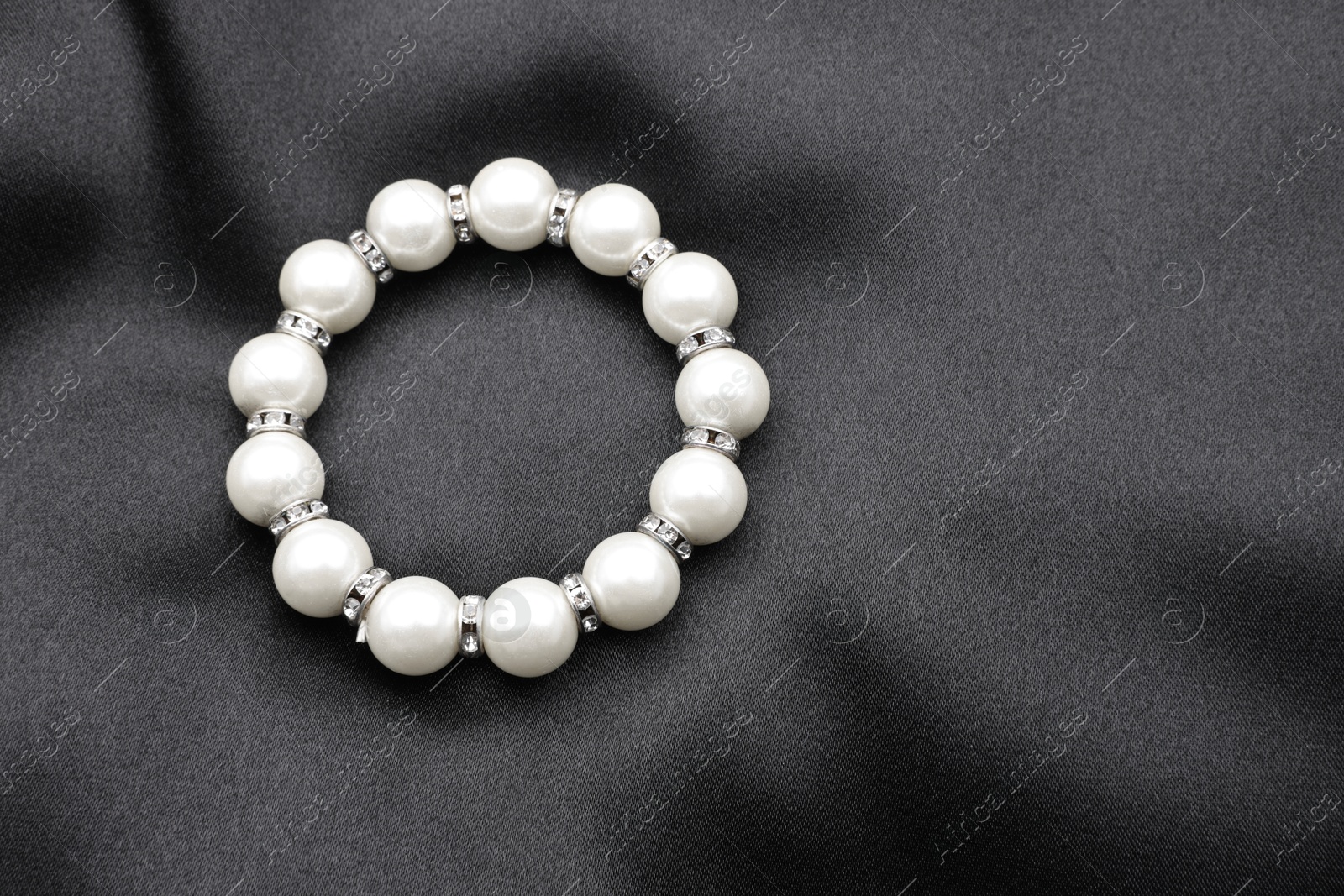 Photo of Beautiful pearl bracelet on black cloth, top view. Space for text