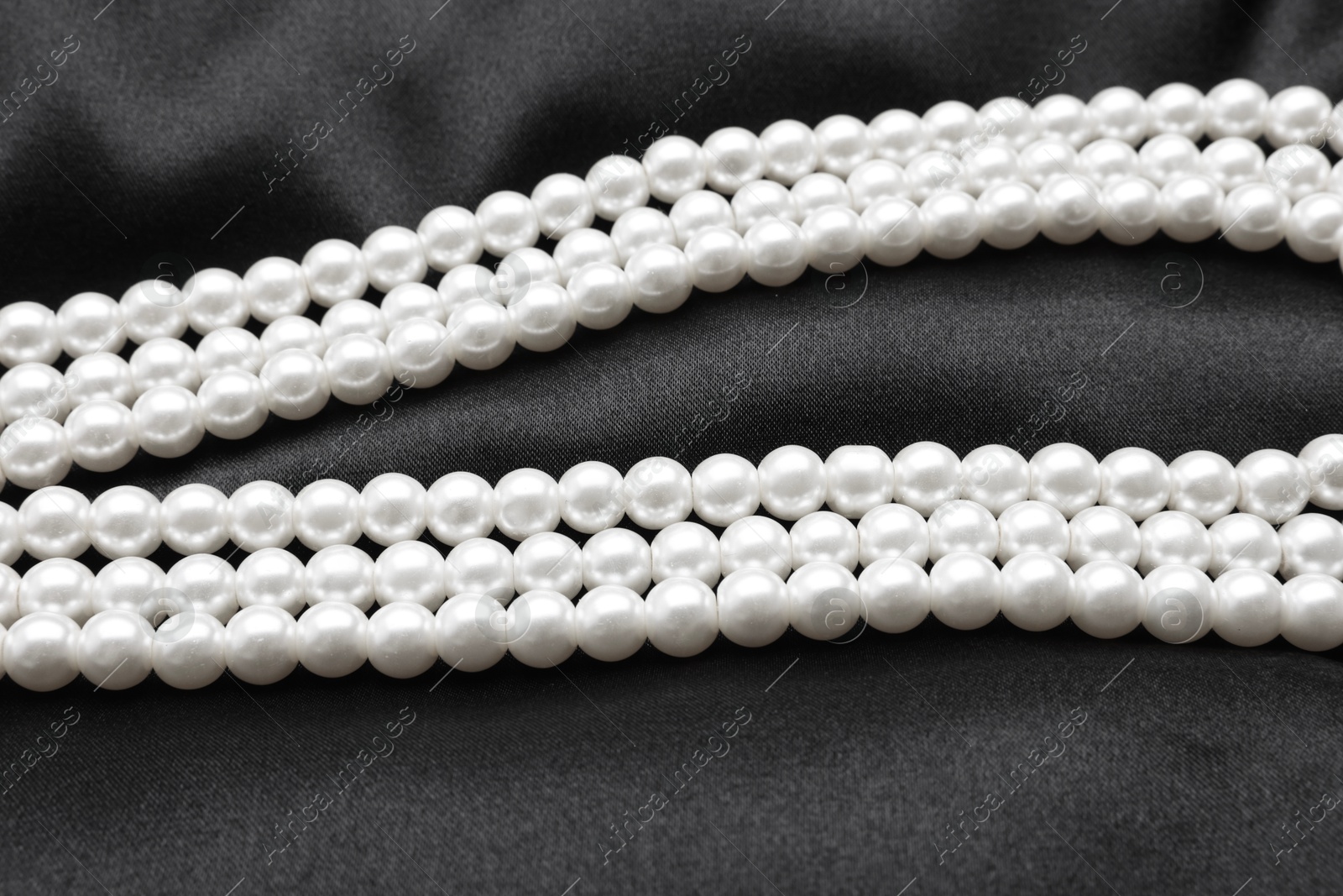 Photo of Beautiful pearl necklace on black cloth, closeup